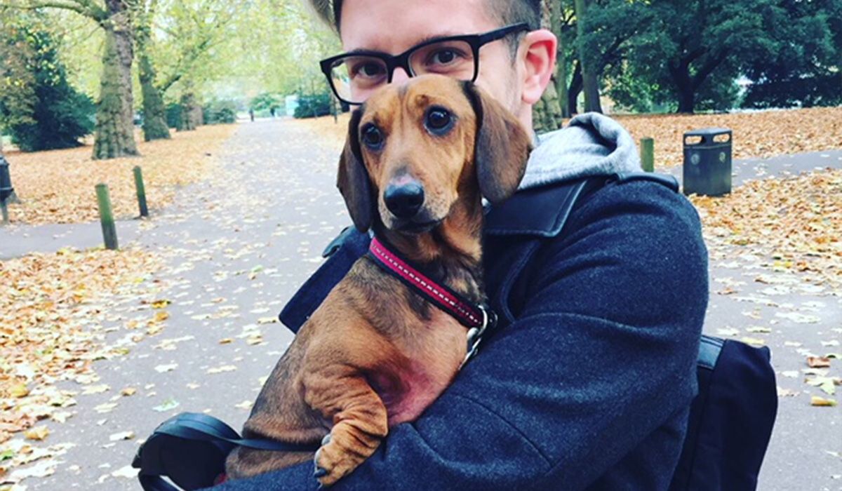 Sam holds Oscar in his arms in a park on an autumnal day
