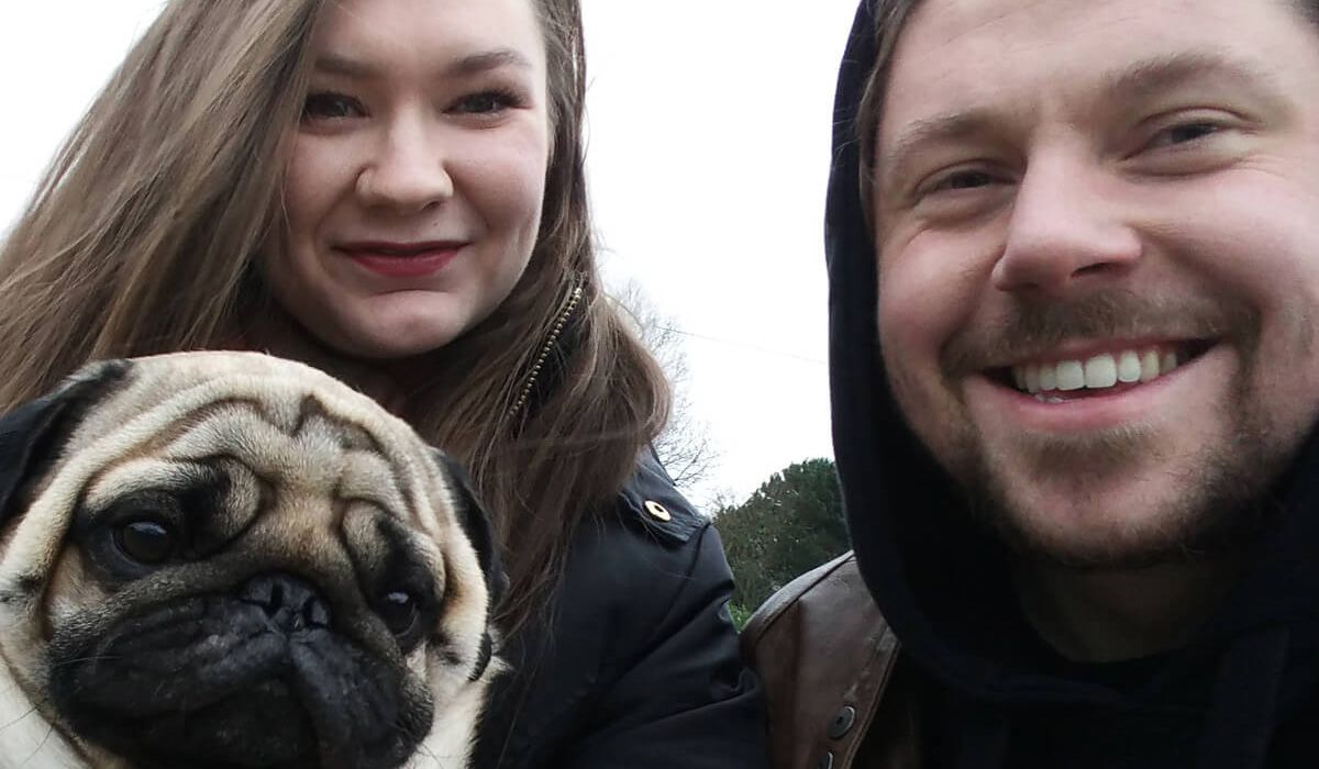 Two smiling people pose with a pug