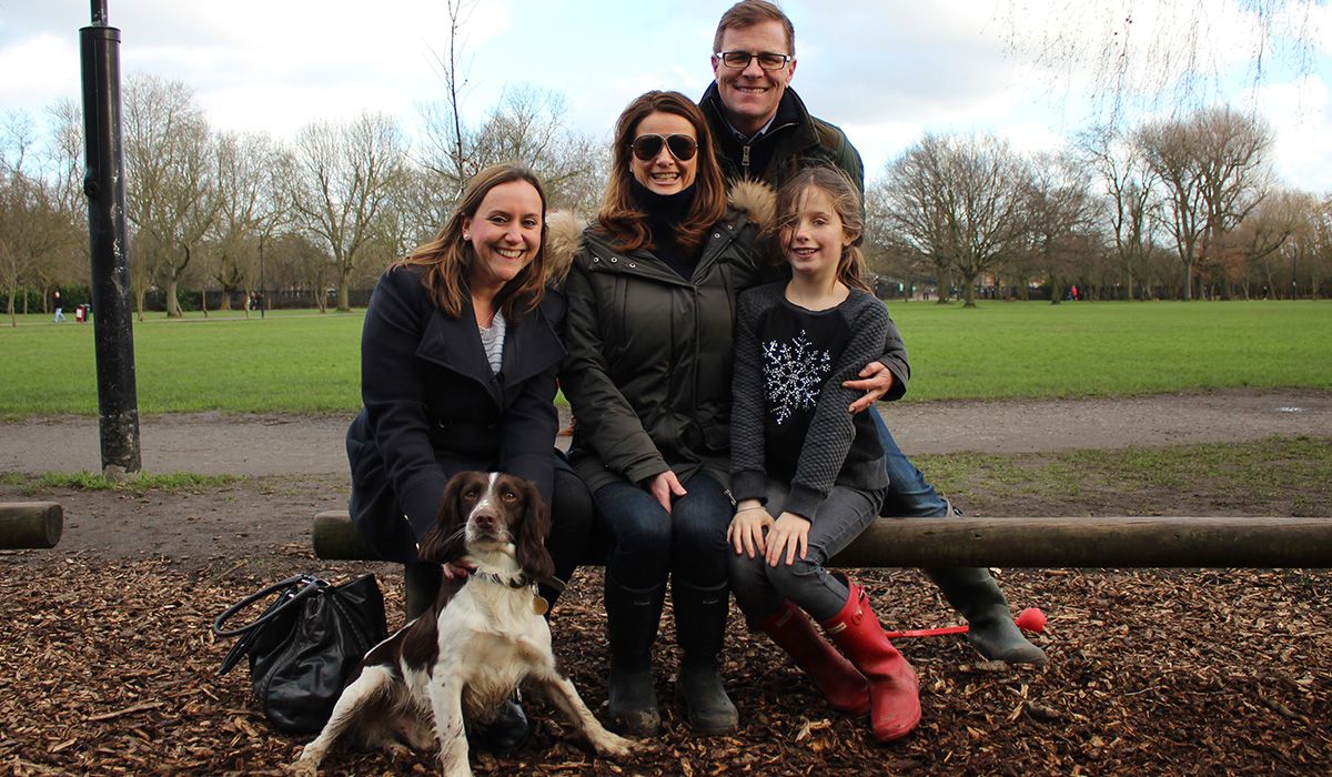 Three adults and a child are sitting in the park together with a brown and white dog