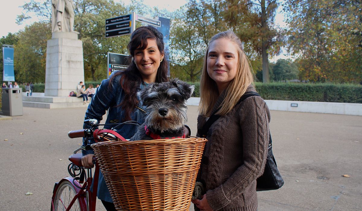 Fuggle is in a wicker bike basket. Standing with him are two smiling women.