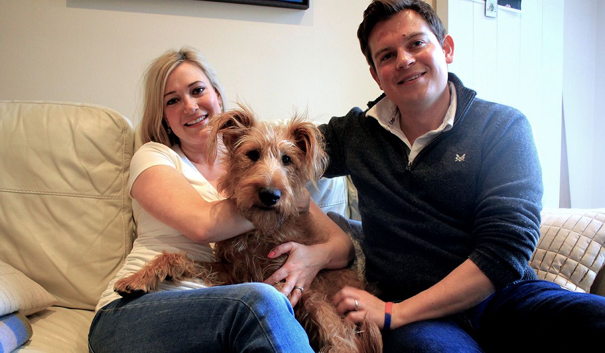 Frank the dog is on the sofa, flanked by his two favourite humans. All look happy and relaxed.