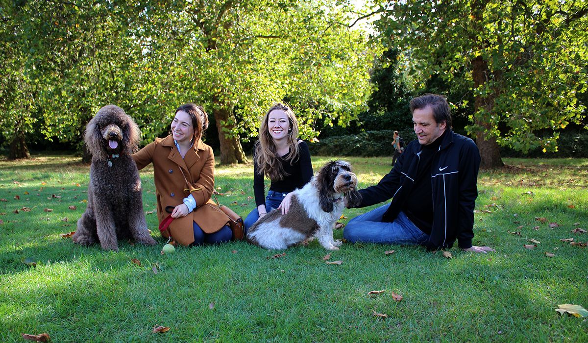 Three people and two dogs all look relaxed and happy in a park on a sunny day