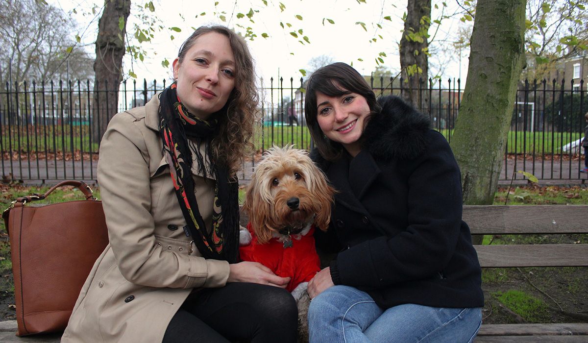 two women on a bench in Highbury Fields with a lovely Cockapoo in a red jacket