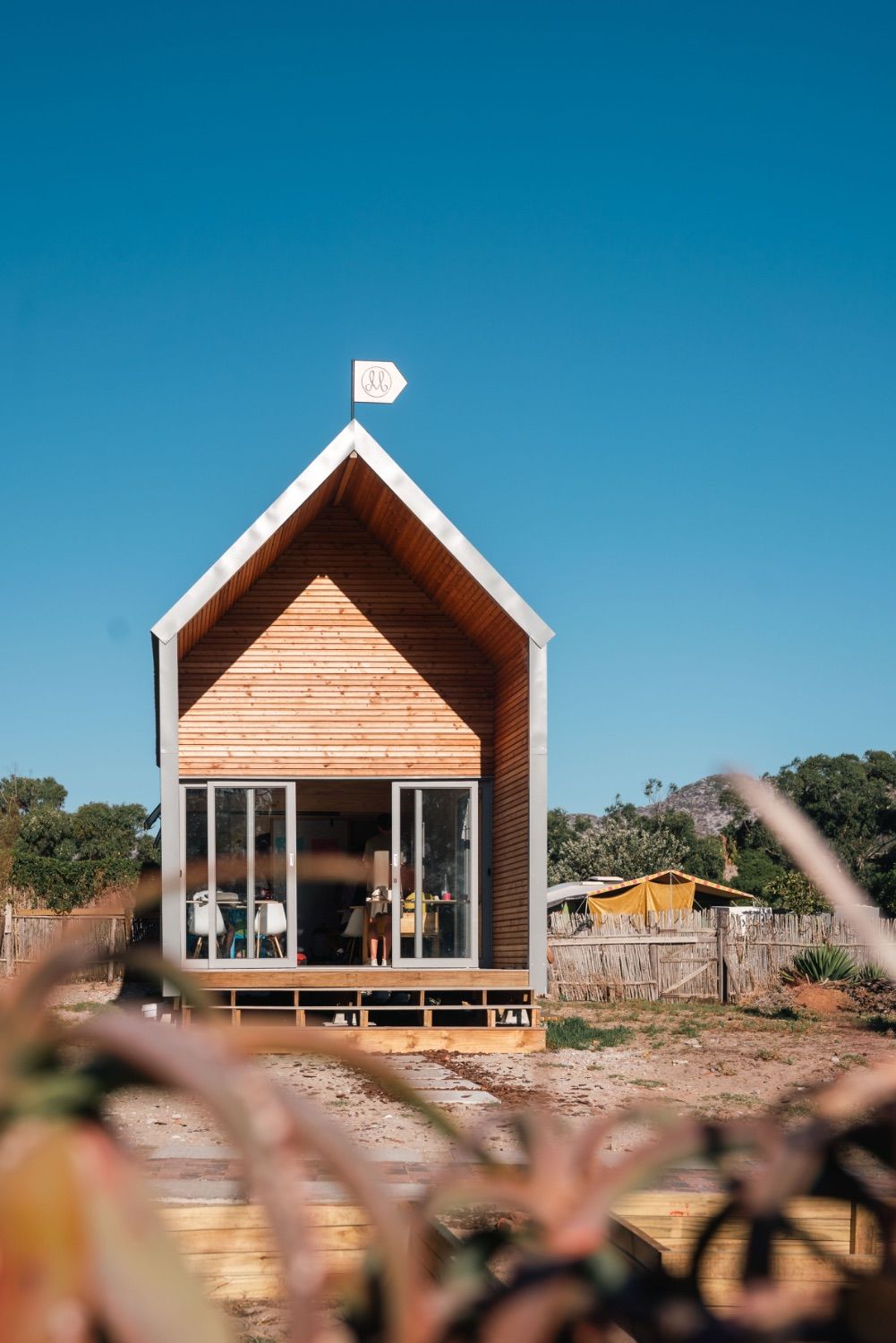 A small timber house with a pitched roof and a flag, under a blue sky