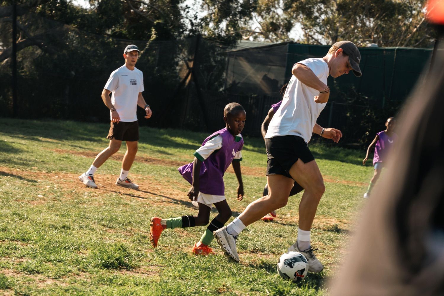 Volunteers playing football with local children on a grass pitch