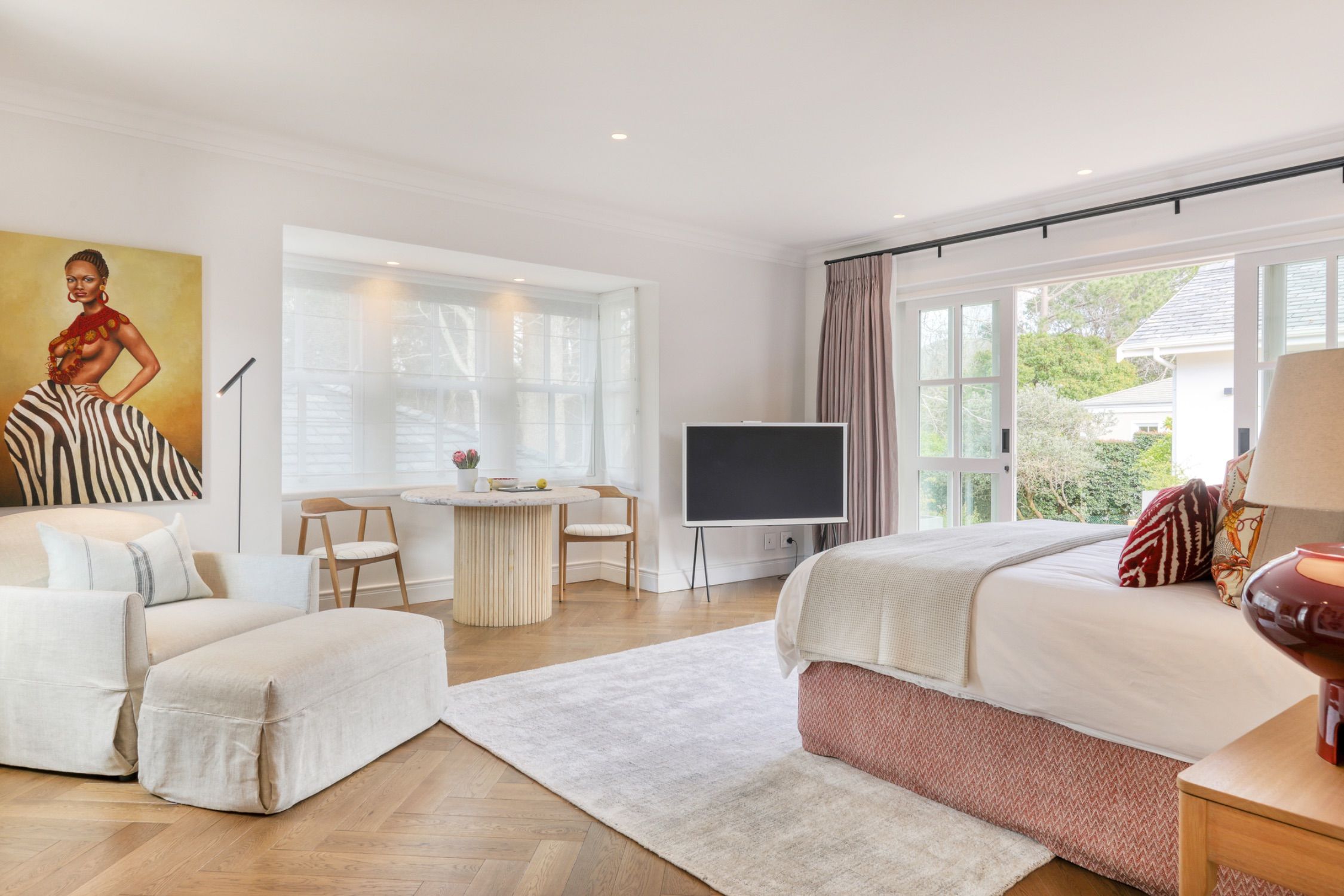 A bright suite with a bed, a sofa and glass doors opening onto the garden