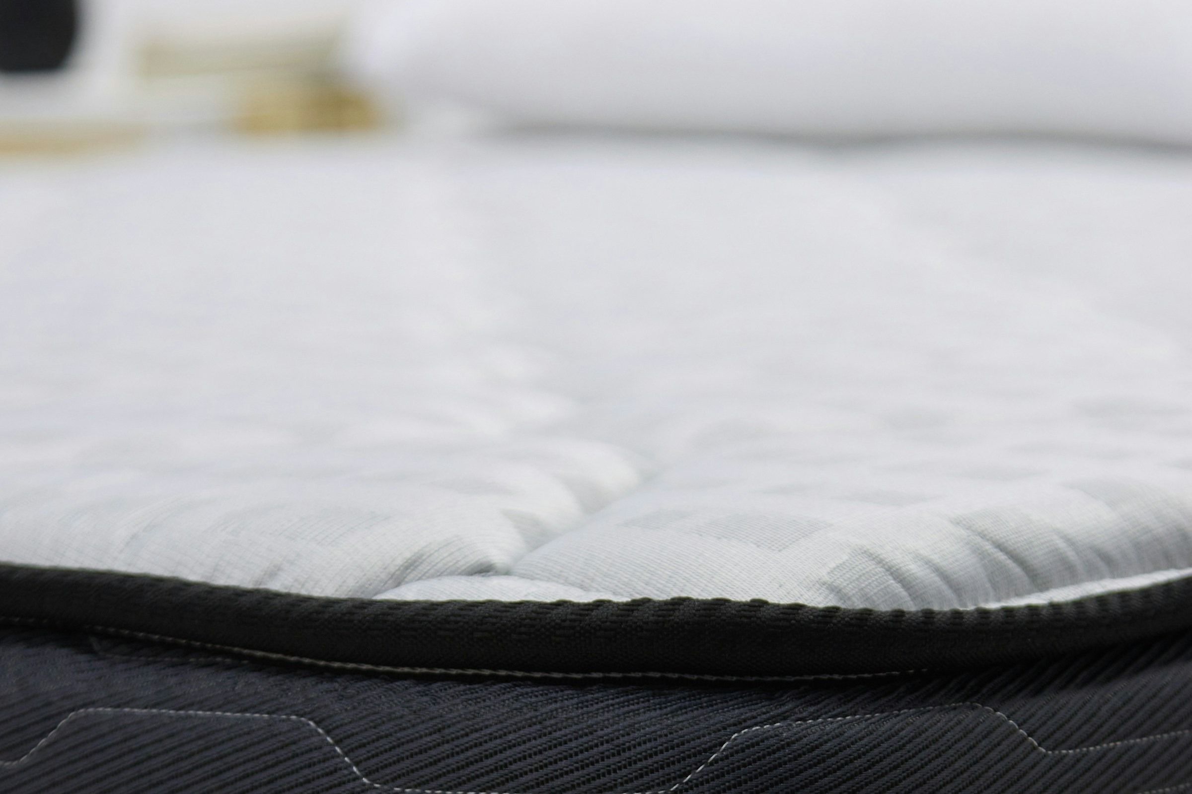 Close-up of a quilted white mattress top with a dark piped edge