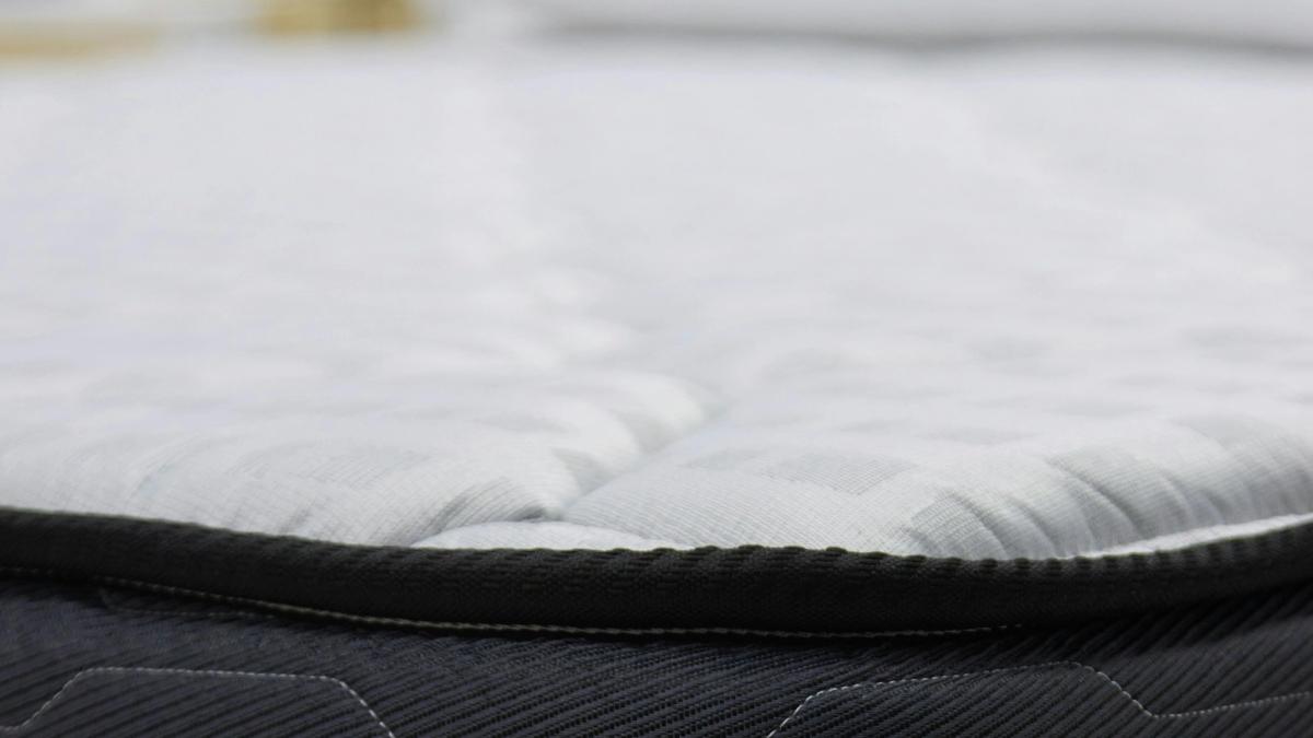 Close-up of a quilted white mattress top with a dark piped edge