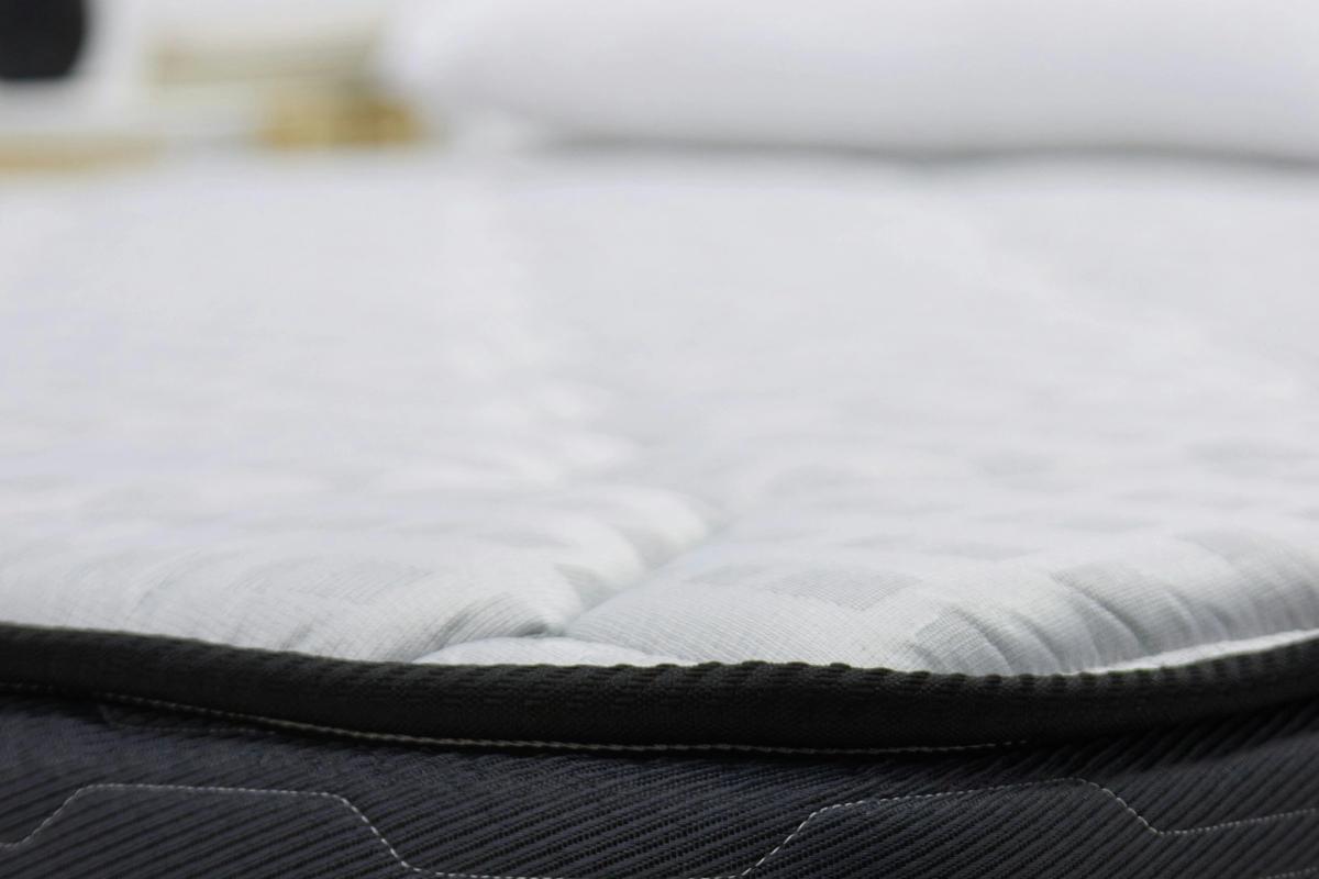 Close-up of a quilted white mattress top with a dark piped edge