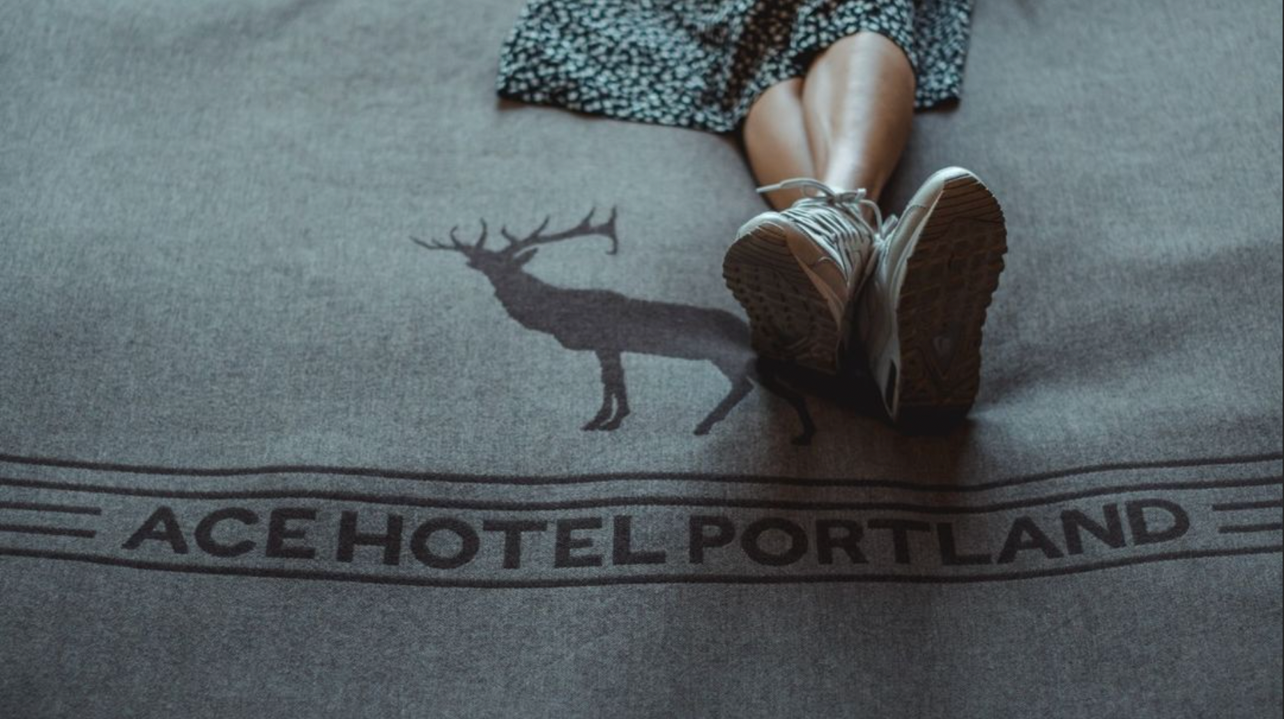 A close up of a persons feet kicked up on bed with a an Ace Hotel Portland wool blanket.
