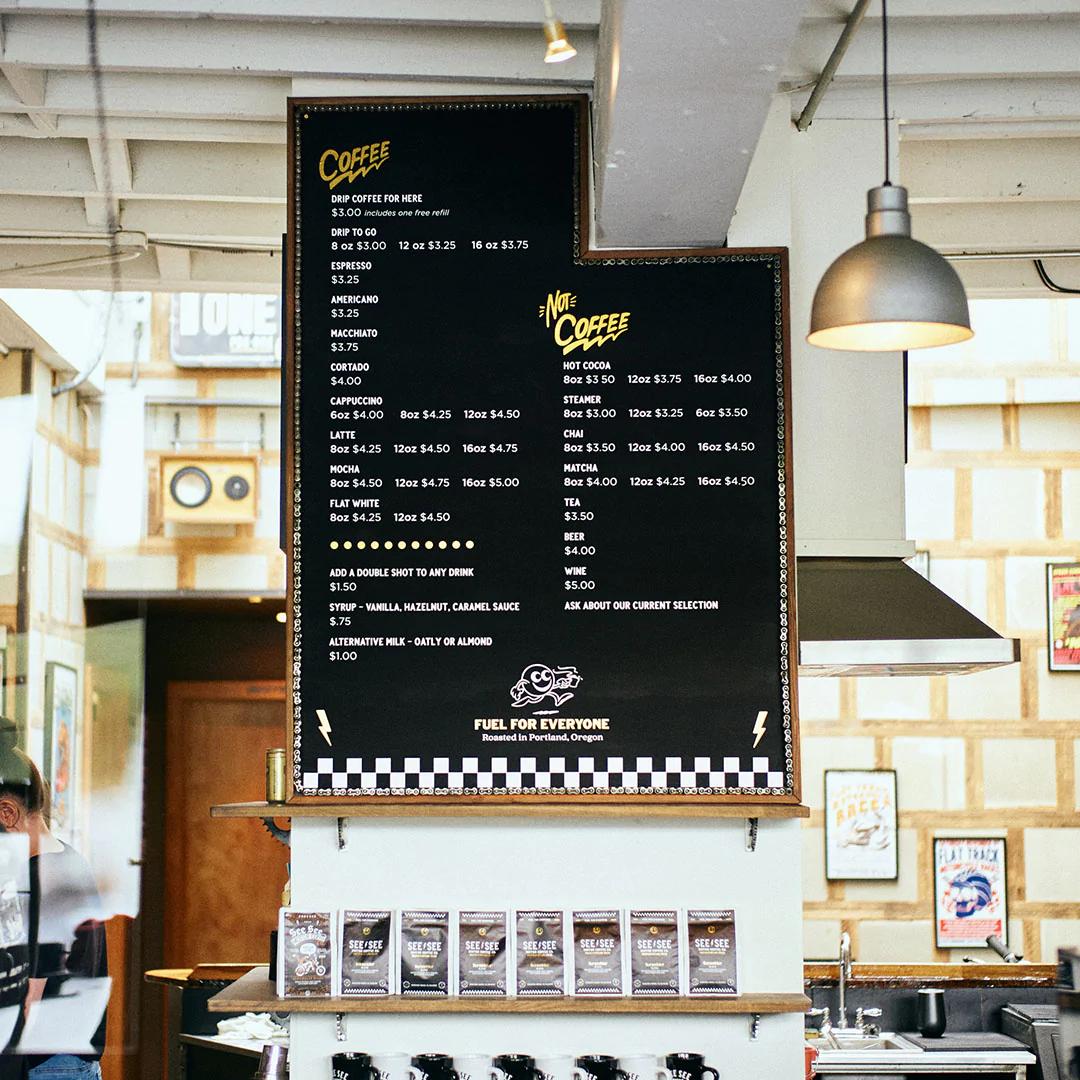 Interior of a See See coffee shop featuring a custom coffee menu on the wall.