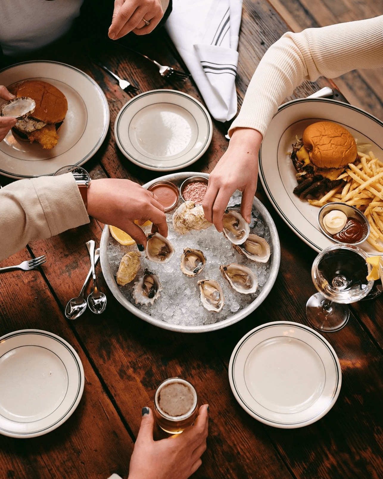 An overhead view of a table top where hands are reaching for oysters on a platter. 