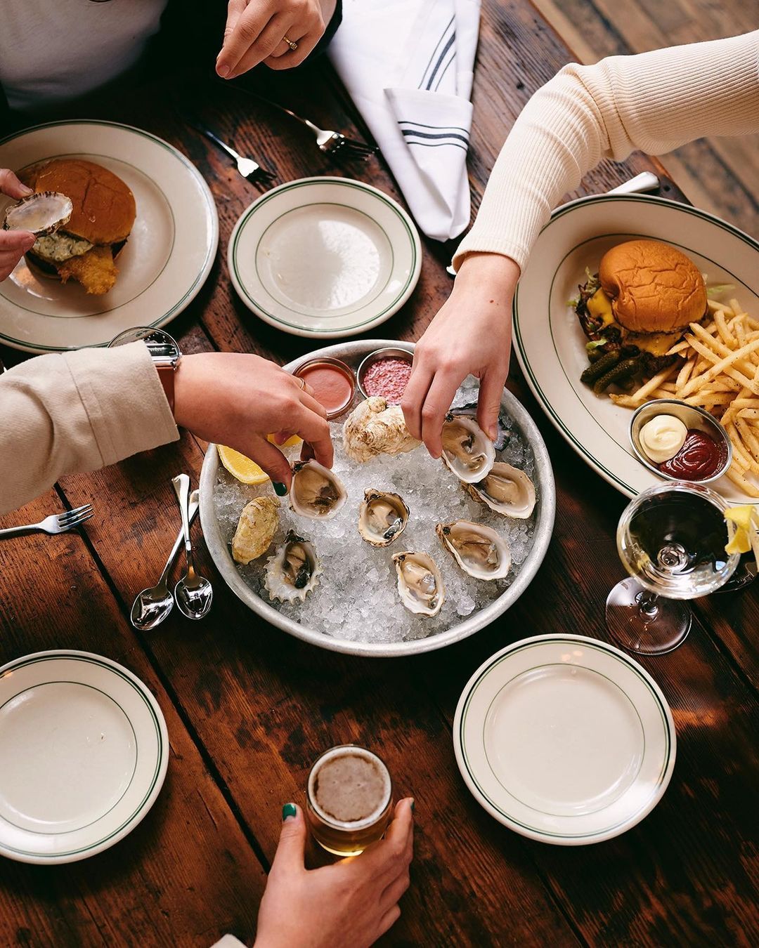 A couple each grab for an oyster from a beautiful spread of oysters on ice at Woodsman Tavern.