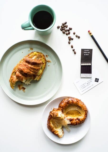 Top down view of a cup of coffee, a breakfast sandwich with a bite taken out of it, a matchbook, and a pastry on a white tabletop