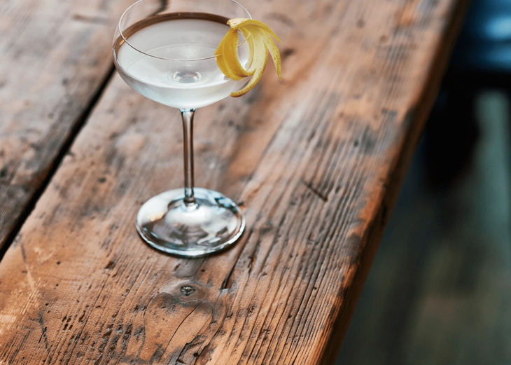 A cocktail in a martini glass on a rustic wood table. 