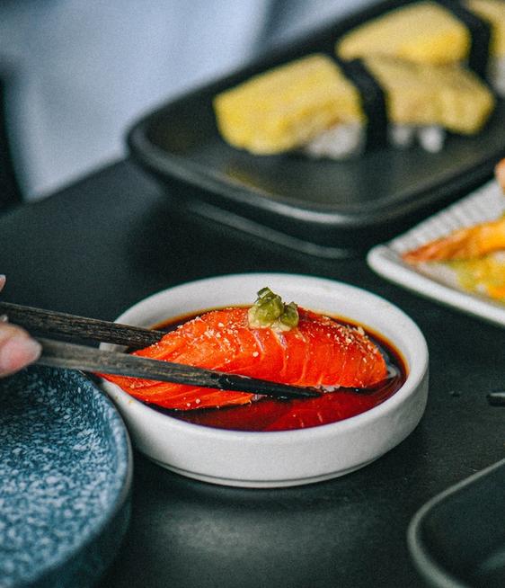 The hand of a chef garnishing a plate of salmon nigiri with blood orange. 