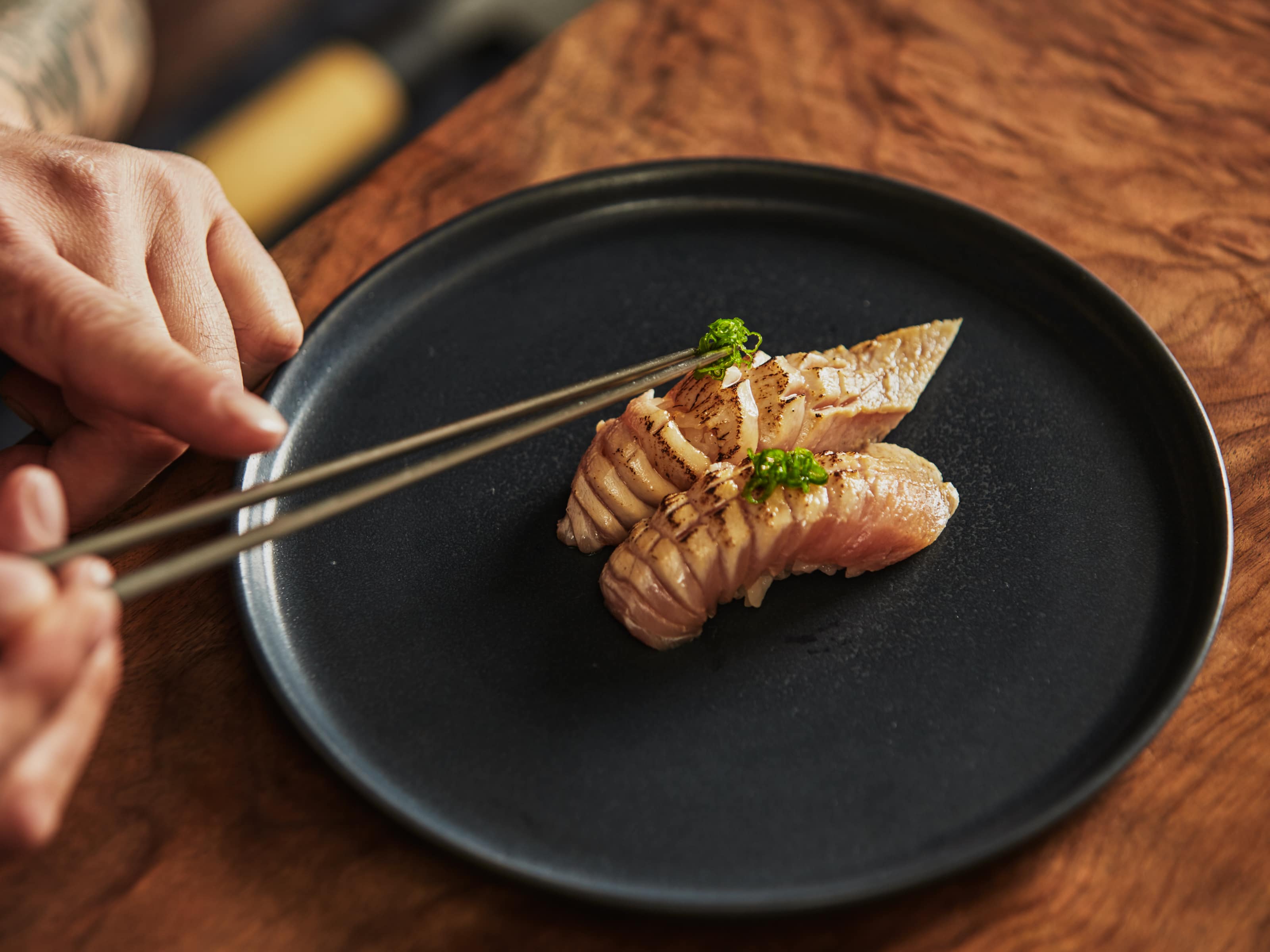 Close up of a chefs hand carefully placing a garnish on a plate of sushi. 