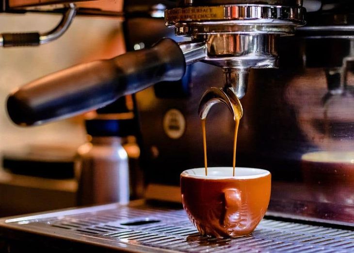 An espresso machine pouring rich brown espresso into a brown demitasse cup