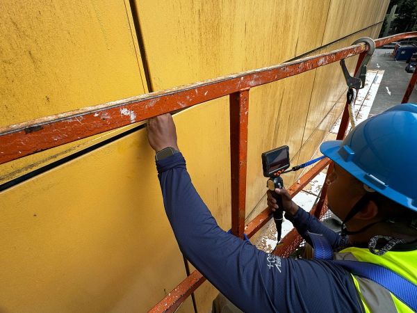 Technician inspecting a yellow facade wall with a borescope camera