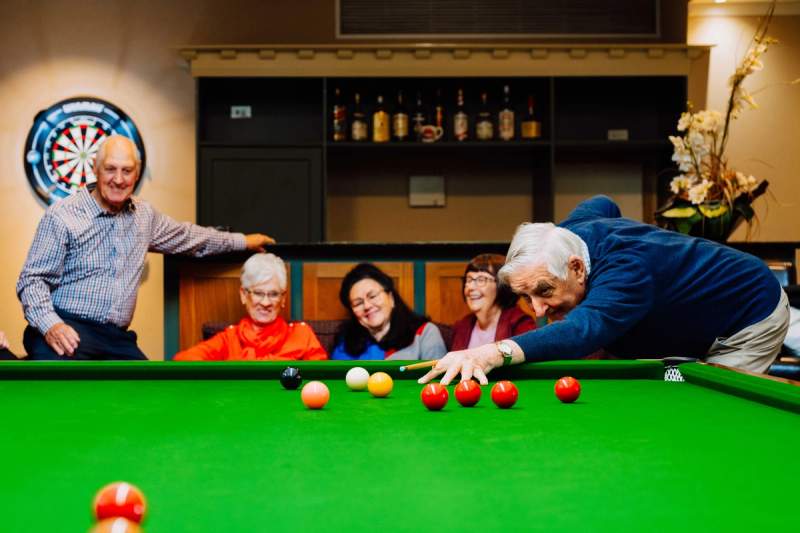 Man lining up shot on pool table while 3 women and a man look on