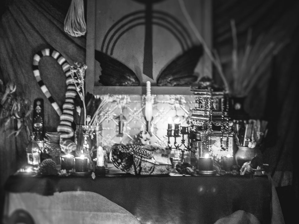 A slightly blurred image of a shrine with candles, flowers in vases and other oddities. 