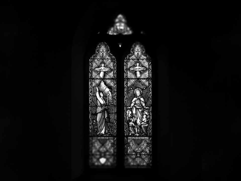 A stained glass window lit from behind, surrounded by darkness.