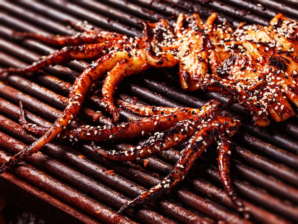 Two chargilled squids on the grill, covered in sesame seeds. 