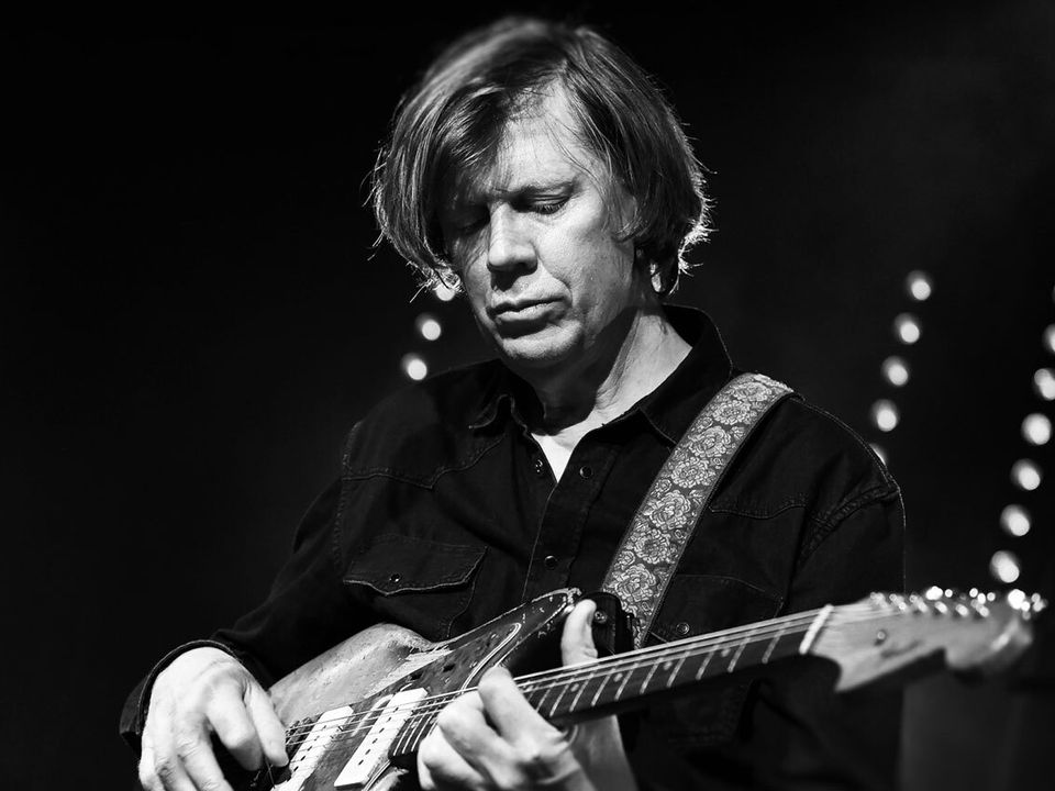 Thurston Moore, seated, playing guitar.