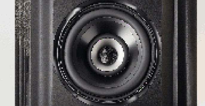 Close-up of a black matte subwoofer with a detailed speaker cone and enclosure, highlighted by soft lighting.