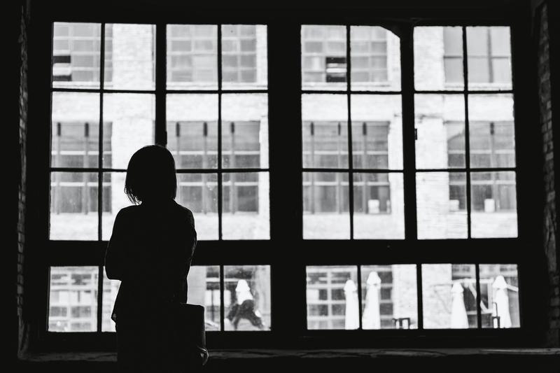 Girl standing at bright window in dark room