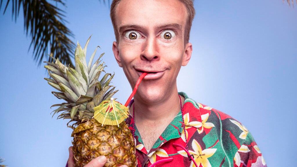 Mand i blomstret hawaii-skjorte som drikker af en ananas gennem et sugerør. Han har store øjne.