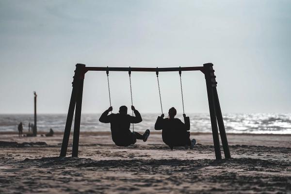 Twee silhouetten op schommels aan zee