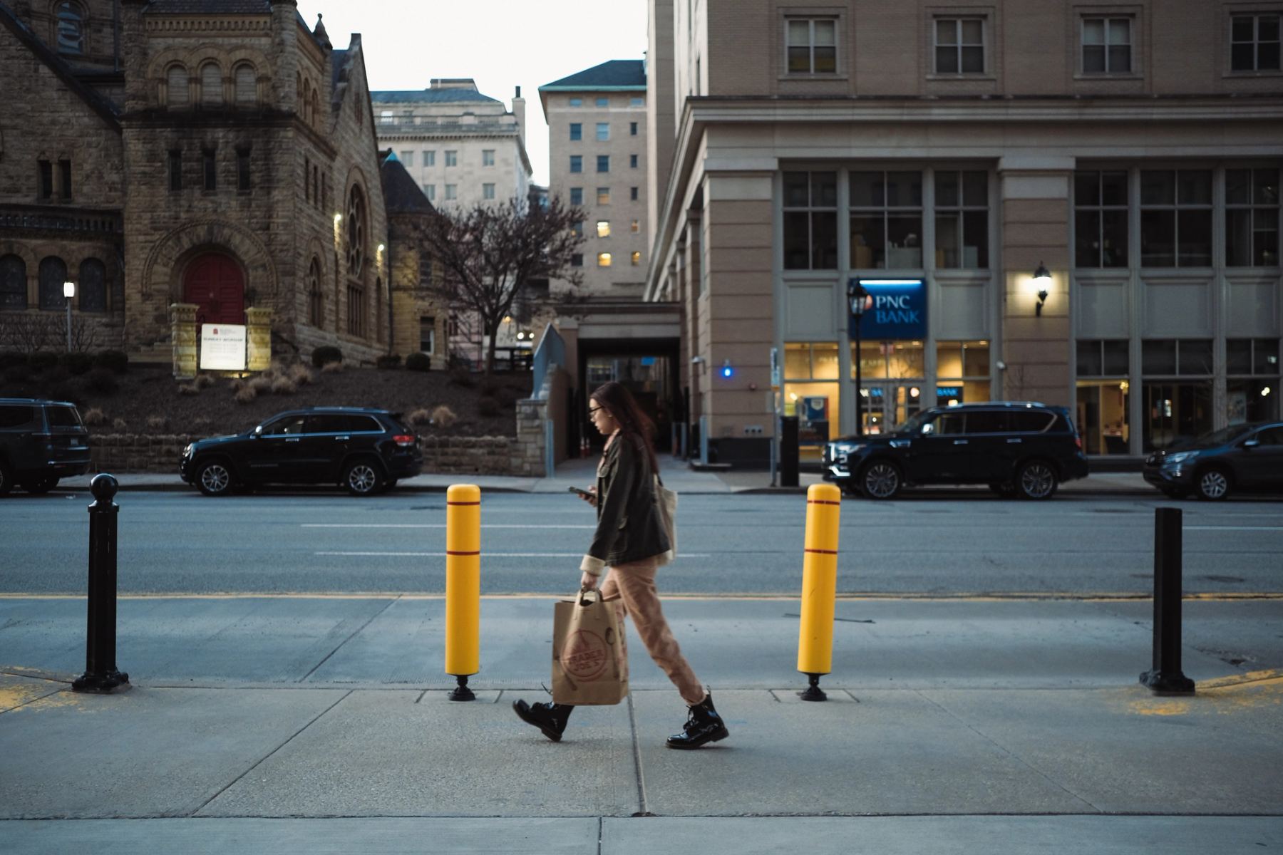 A lady walking on the side of a road, holding a paper bag