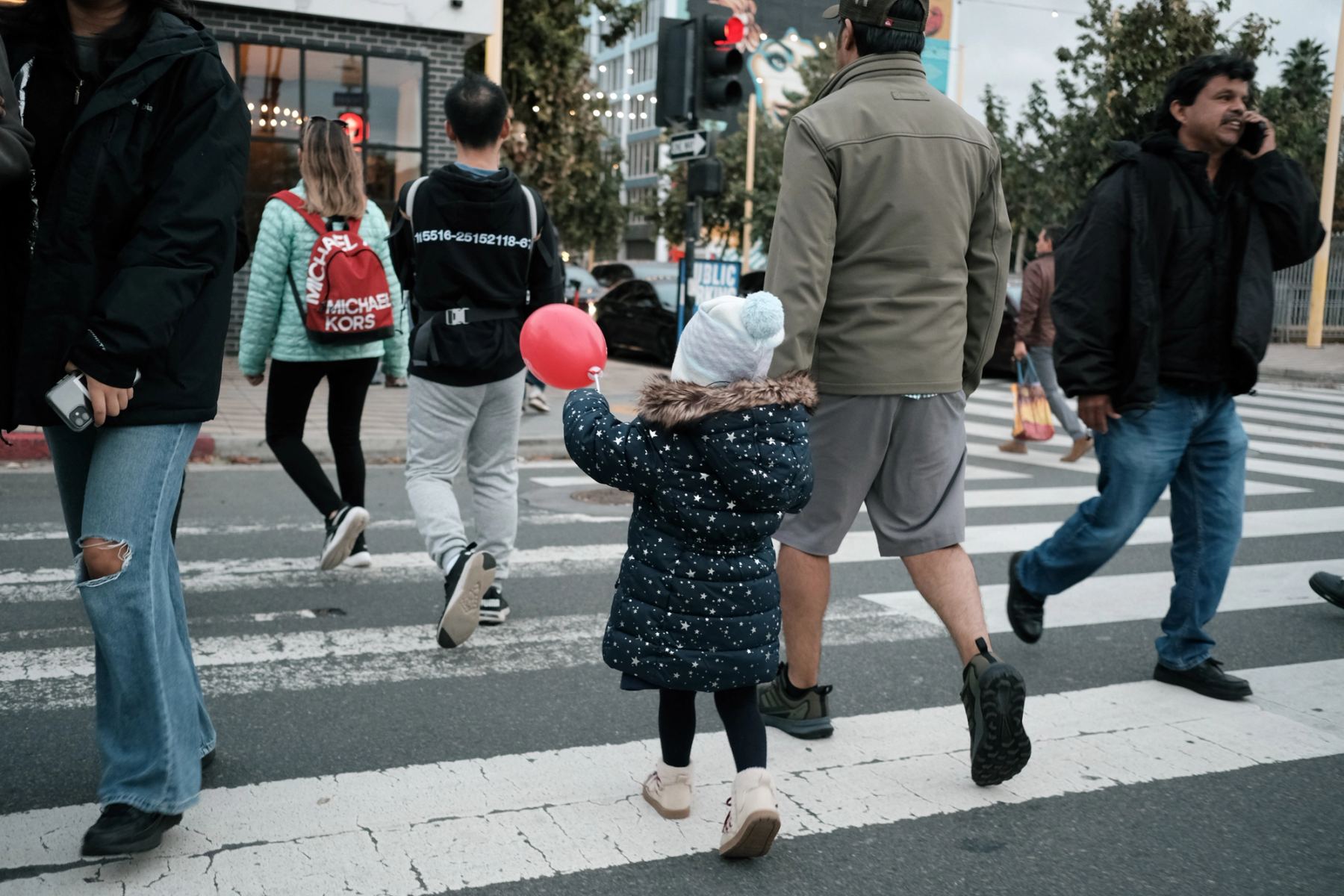 A girl walking across street holding a red balloon