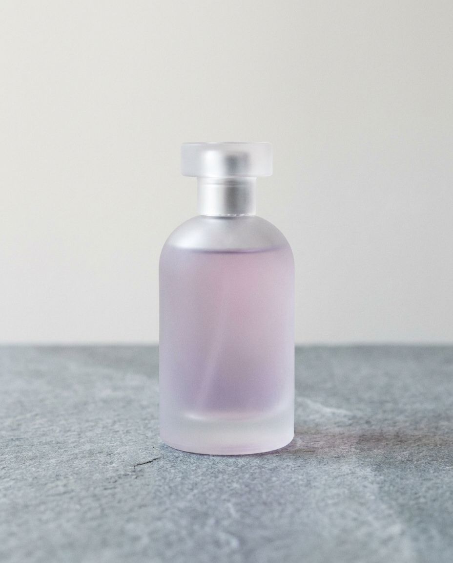 Frosted glass perfume bottle with pale lilac liquid on stone