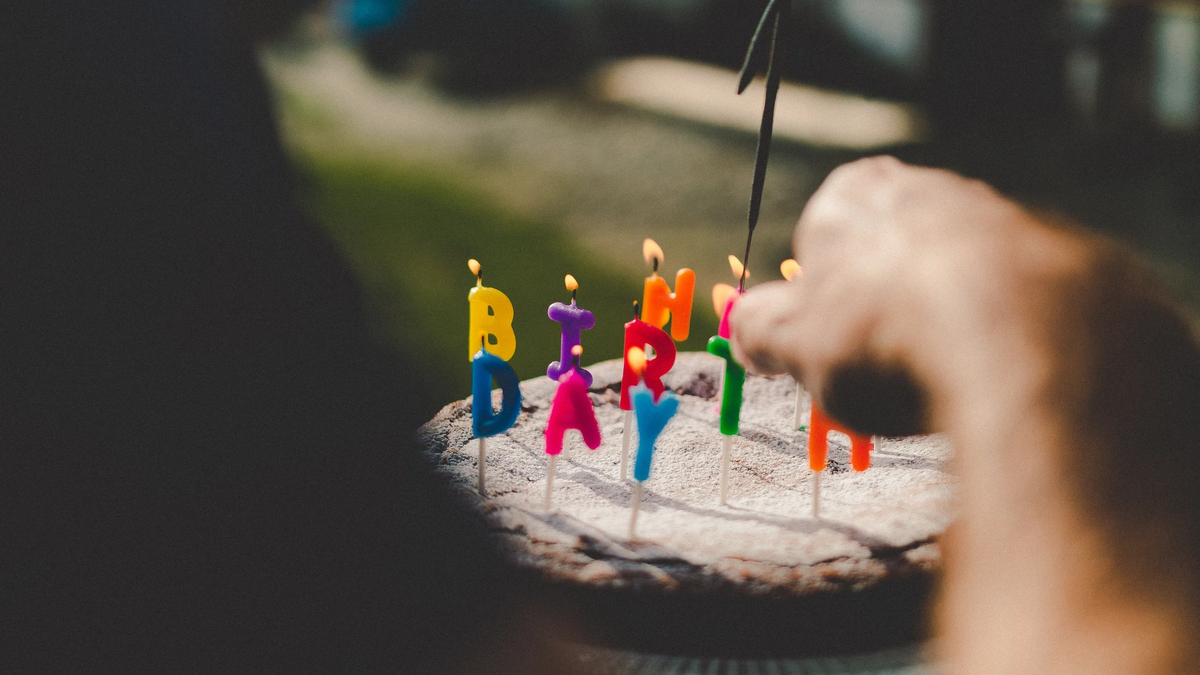 A hand lighting a candle on a cake decorated with letter candles spelling out Happy Birthday