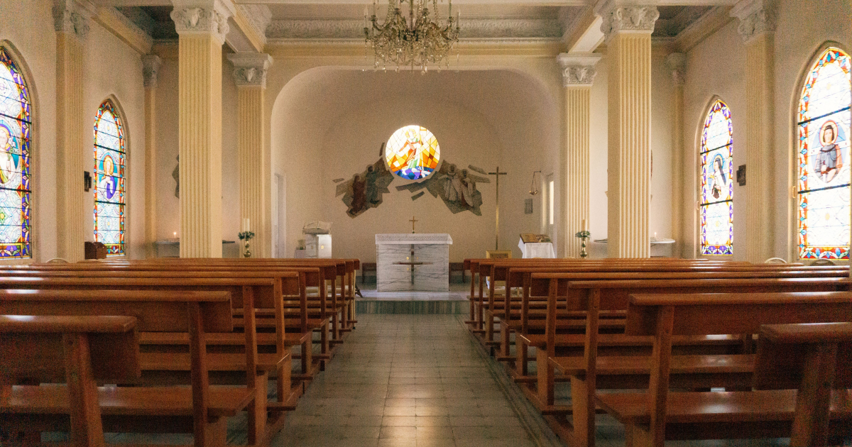 Interior de igreja com bancos de madeira e vitrais coloridos nas janelas.