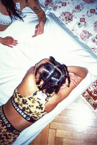 Woman in a camo bodysuit laying on the bed w her friend. Converse X Faith Connexion, Koché, Feng Chen Wang collaboration