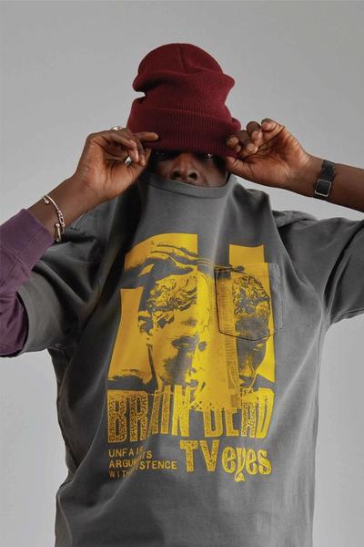 Man wearing chuck 70s, black chinos, green sweatshirt w gorilla embroidery around his waist, black bomber / hoody and a maroon watch cap beanie. Brain Dead x Converse collaboration.