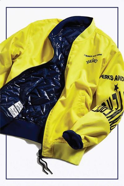 Detailed photo of a reversible bomber jacket the outside of which is bright acidic yellow with graphics on the sleeve and chest, the inside being quilted shiny blue nylon.Converse x P.A.M. (Perks and Mini) collab. 