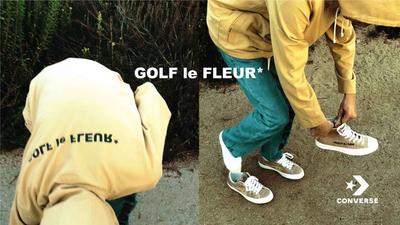 A photo of a man putting on his shoe. while on the beach. tyler, the creator x converse collab