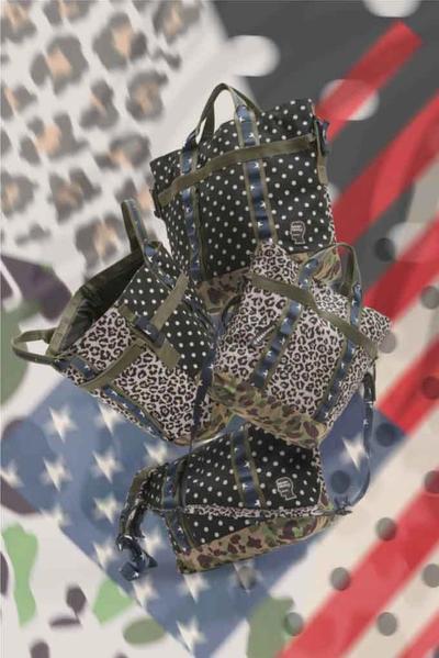 An image of multiple duplicate bags in the air with a background of polka dots, camo and the american flag. Brain Dead x Converse collaboration.
