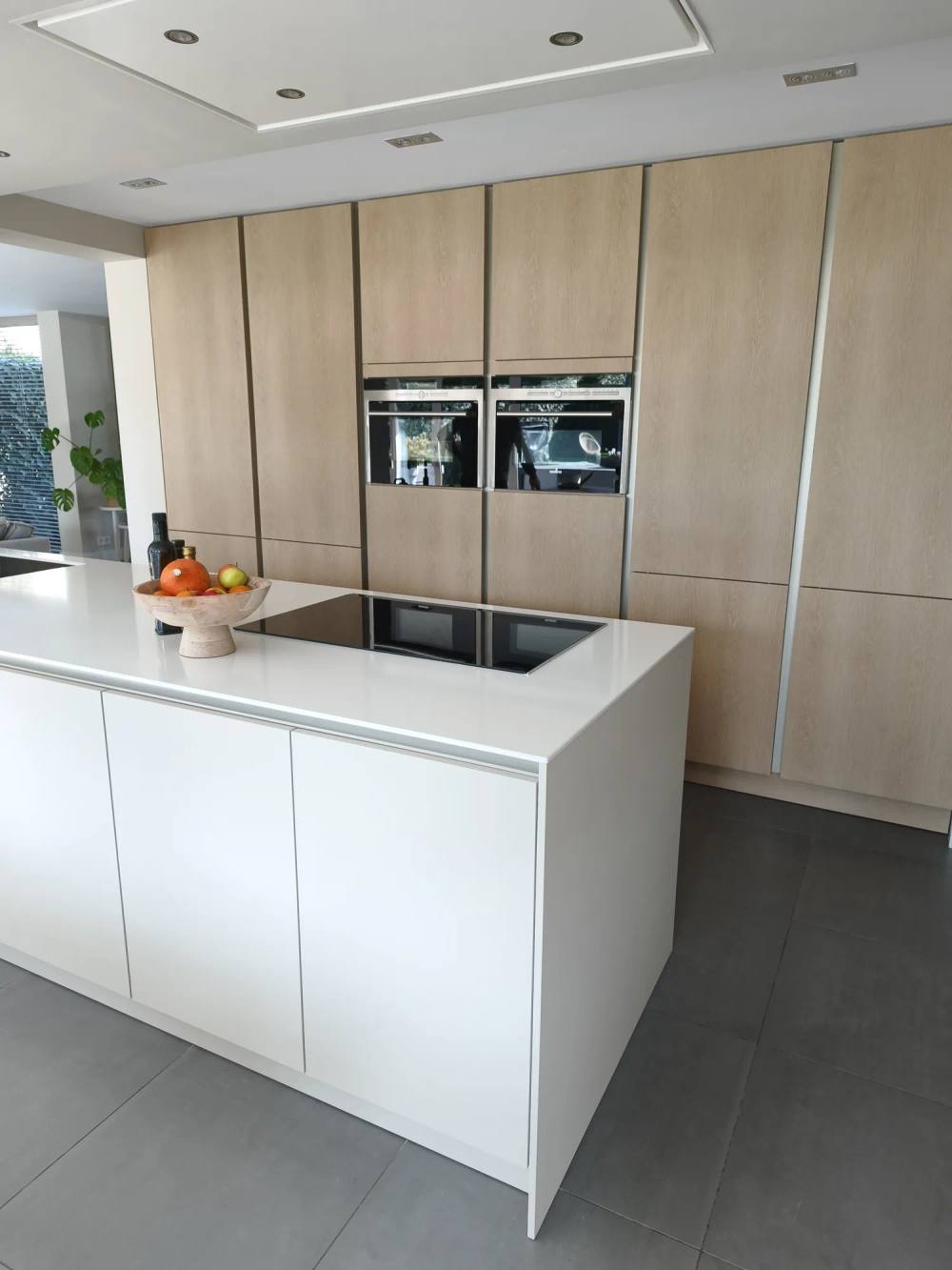 Keuken met een hoge kastenwand in lichte eikenlook en een wit kookeiland
