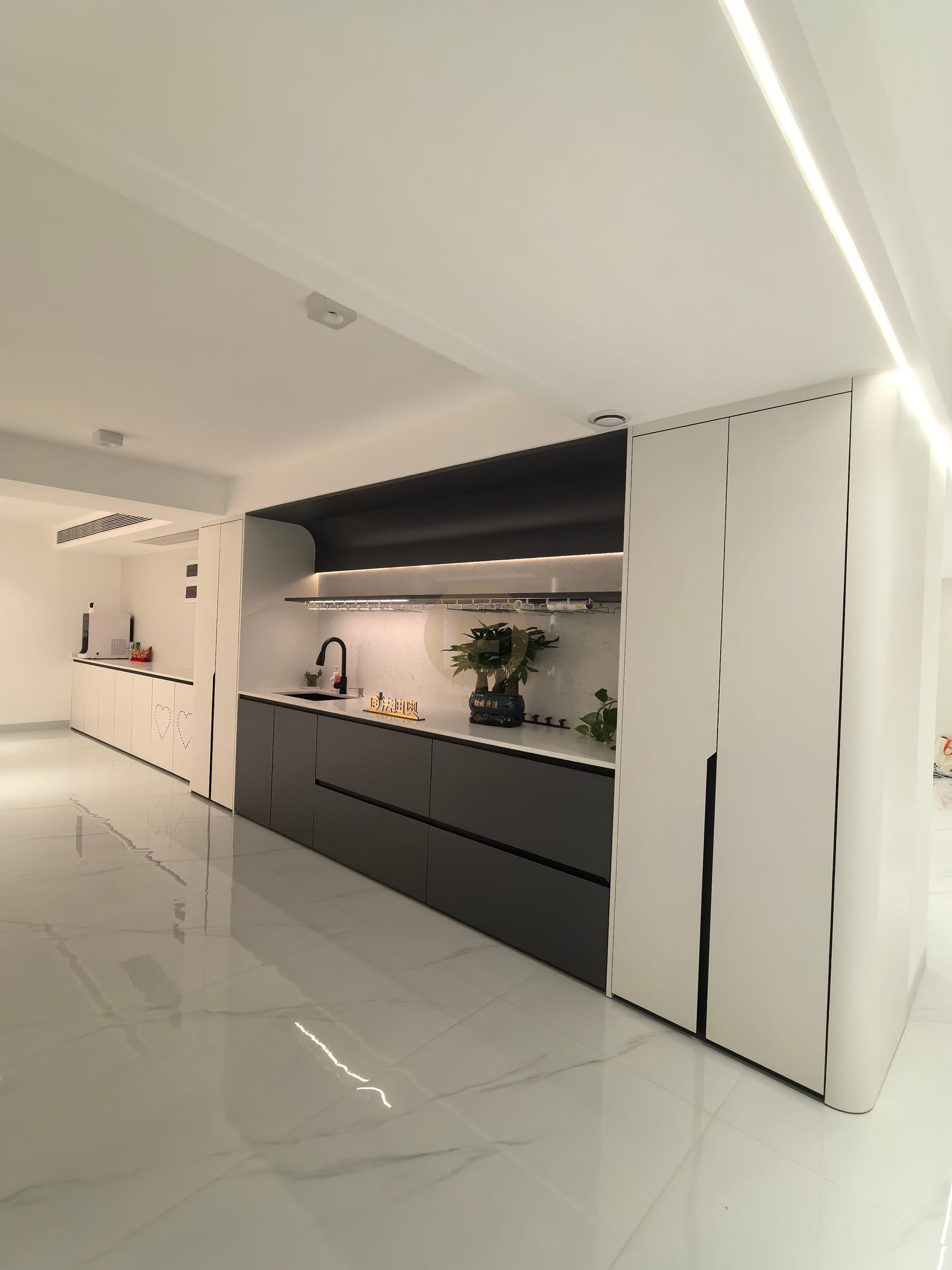Open-plan view of the black-and-white stainless steel bar kitchen with lit shelf and marble floor