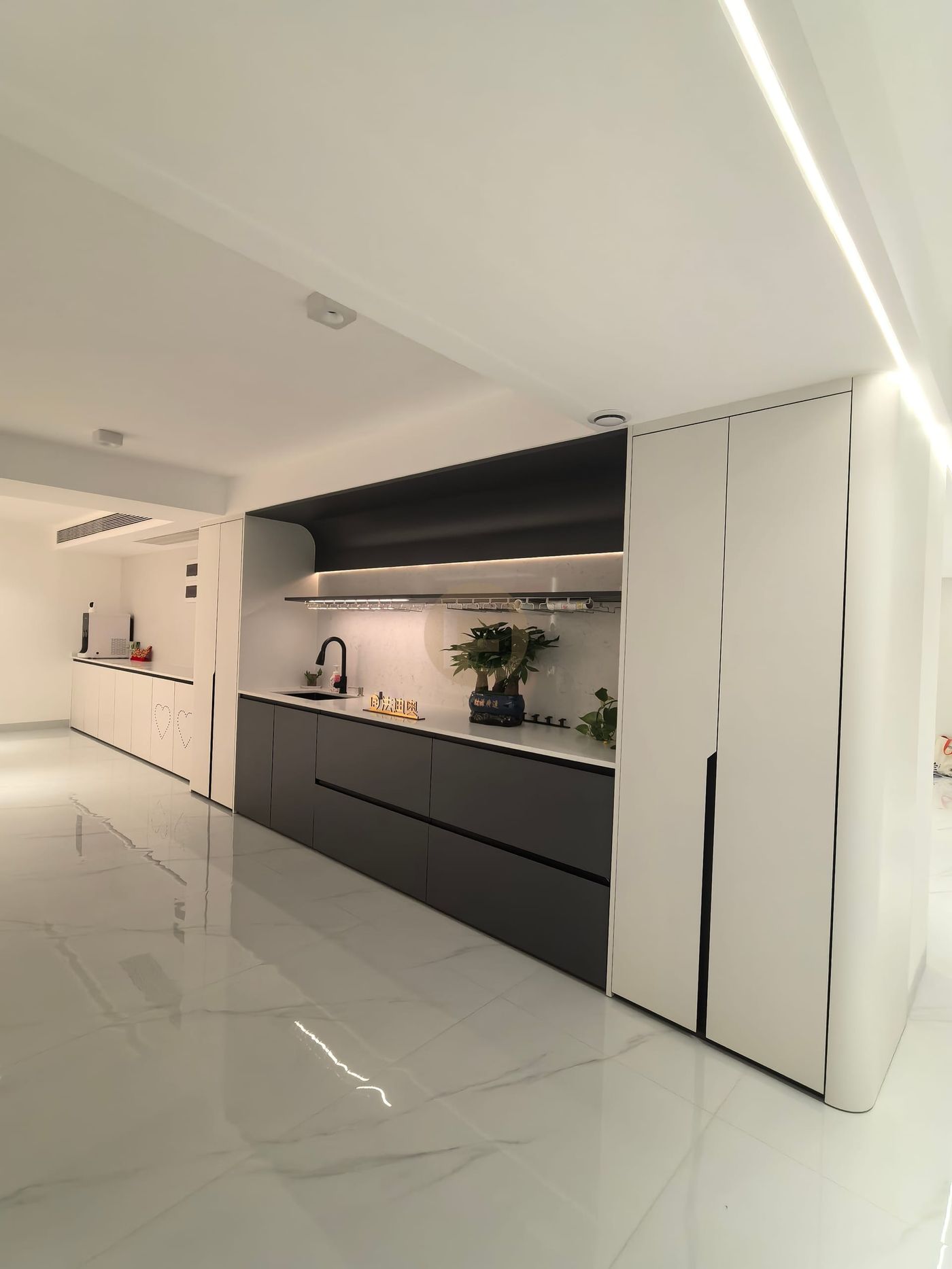 Open-plan view of the black-and-white stainless steel bar kitchen with lit shelf and marble floor