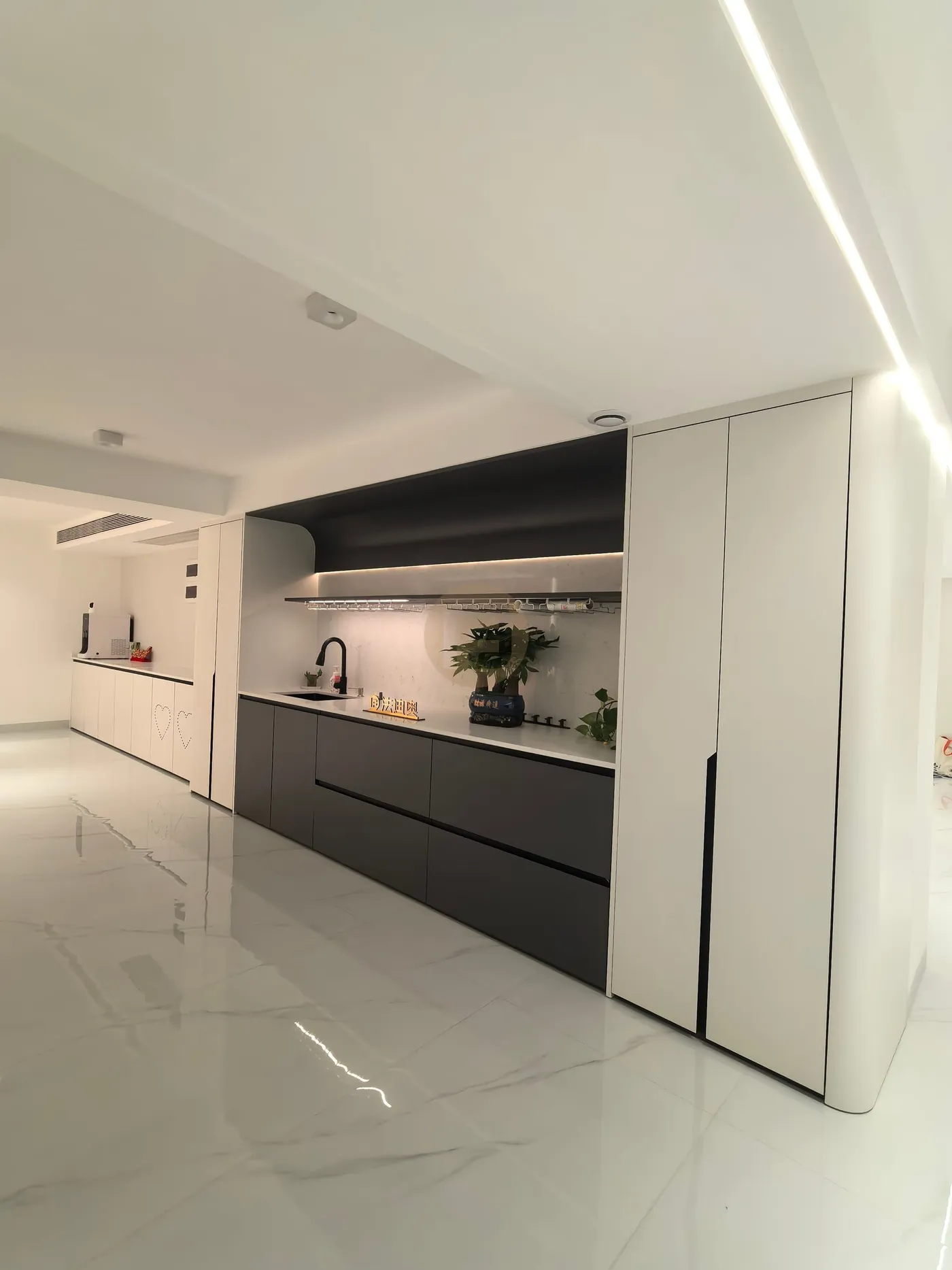 Open-plan view of the black-and-white stainless steel bar kitchen with lit shelf and marble floor