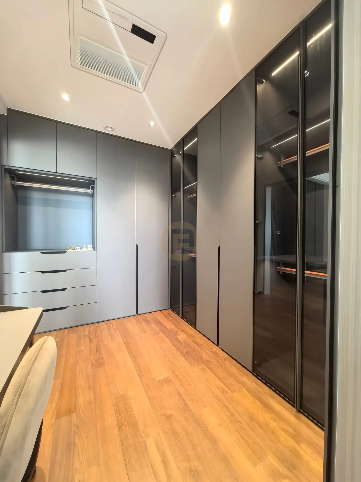 Walk-in closet combining smoked-glass wardrobe doors with matte grey stainless steel drawer units
