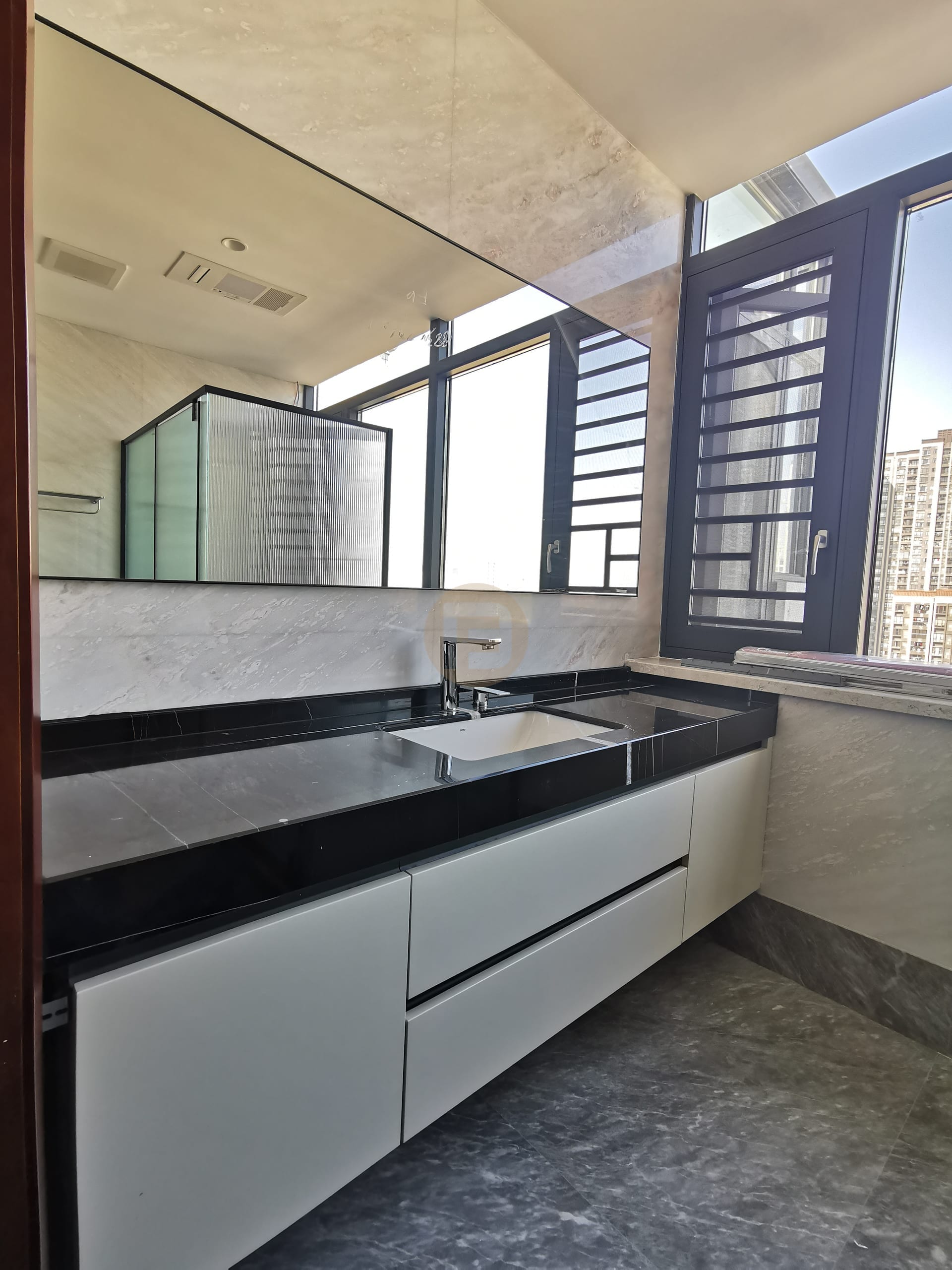 Black stone vanity counter on white stainless steel drawers beneath a full-width mirror and corner windows