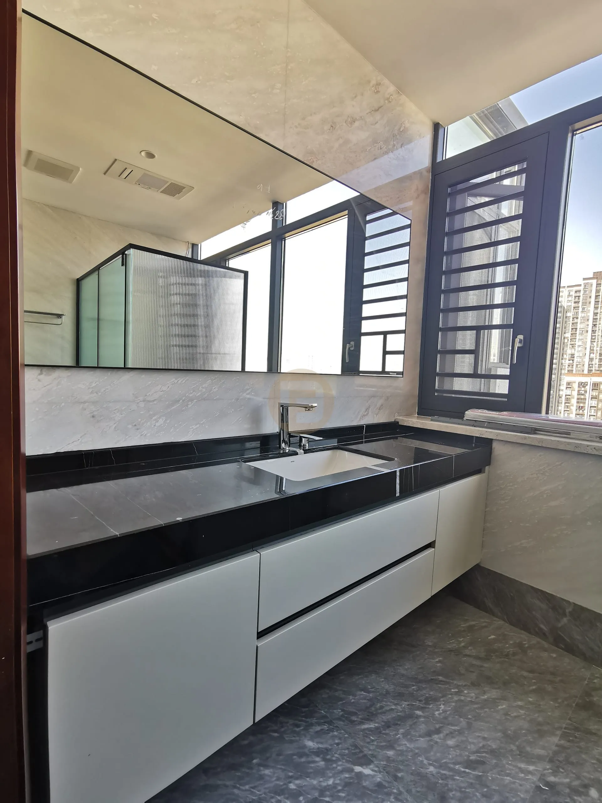 Black stone vanity counter on white stainless steel drawers beneath a full-width mirror and corner windows