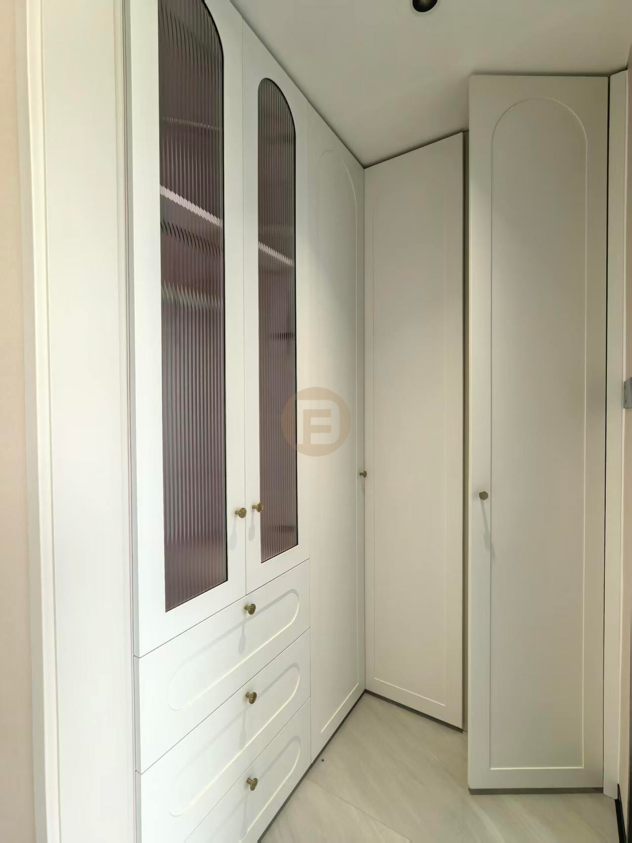 Cream arched wardrobes with reeded-glass doors and brass knobs lining a walk-in closet corner